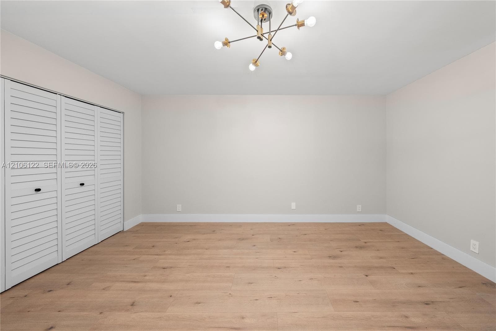 Wood-finish flooring, multi-panel louvered closet doors, and a modern multi-arm sputnik-style light fixture
