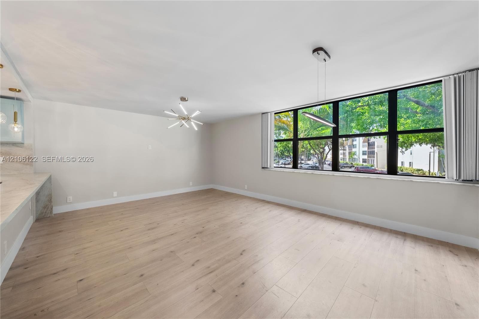 Open-concept interior featuring wood-finish flooring, expansive windows, multi-arm sputnik-style chandelier, and built-in counter space with stone-patterned surfaces