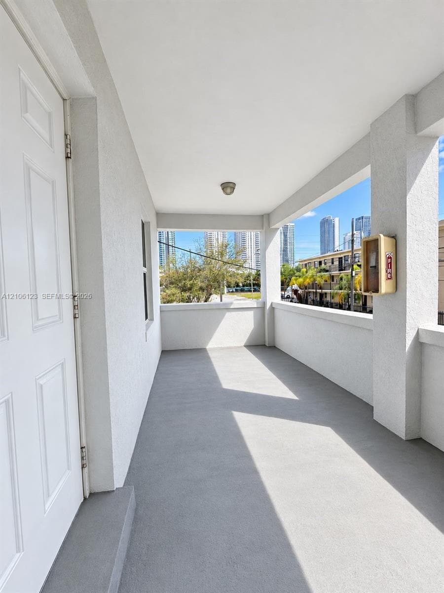 Covered balcony featuring a neutral-toned concrete floor, textured wall finishes, and a high ceiling with a flush-mount light fixture