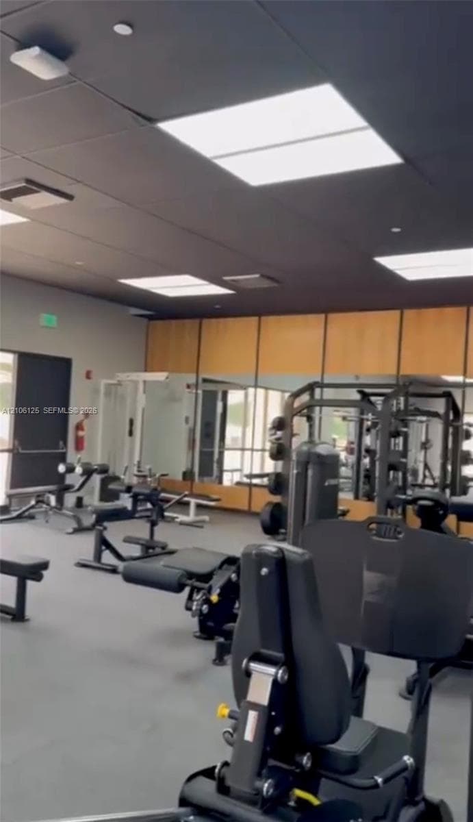 Fitness center featuring a dark-toned ceiling, recessed square lighting panels, wall-to-wall mirrors, and resilient flooring