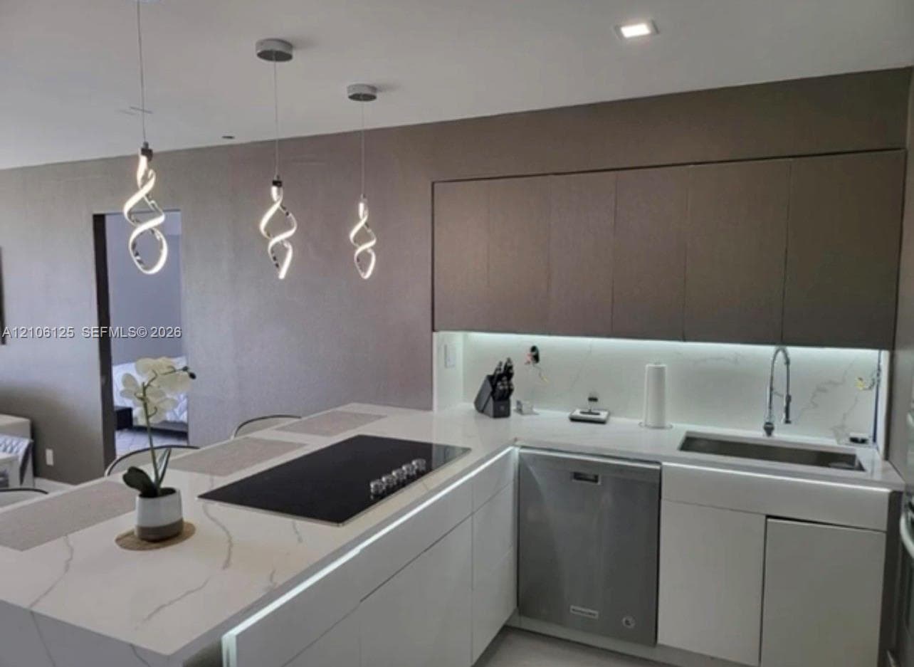 Kitchen featuring quartz countertops with integrated backsplash, flat-panel cabinetry, stainless steel dishwasher, inset cooktop, and three spiral pendant lights