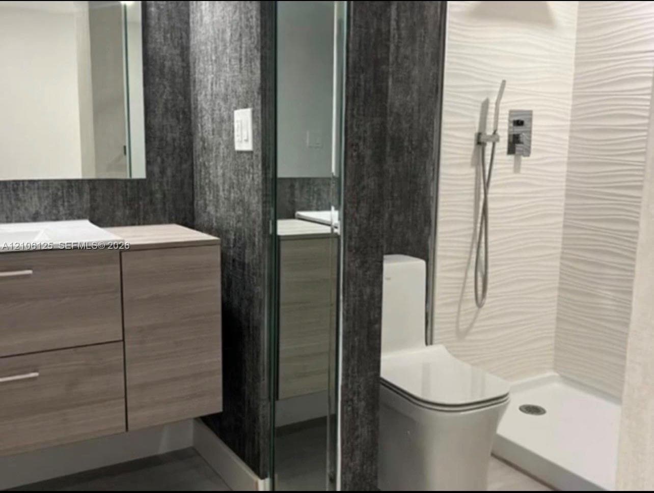 Modern floating vanity with wood-finish cabinetry, white textured wave-patterned shower wall tiling, floor-to-ceiling mirror panel, and wall-mounted hand shower fixture