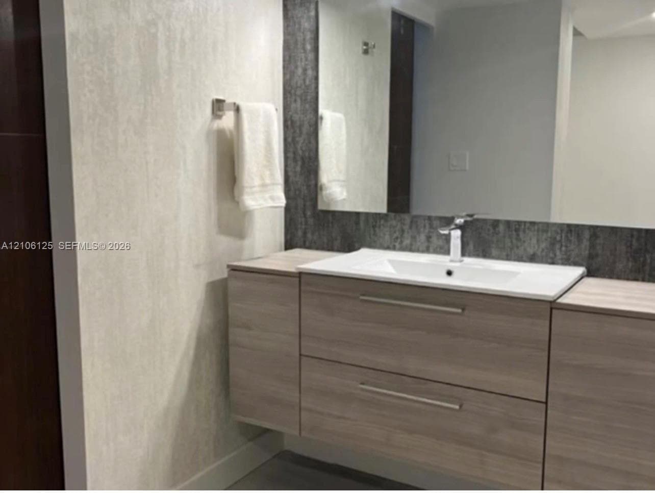 Floating wood-finish vanity with dual storage drawers, integrated white sink, brushed metal hardware, and large frameless mirror