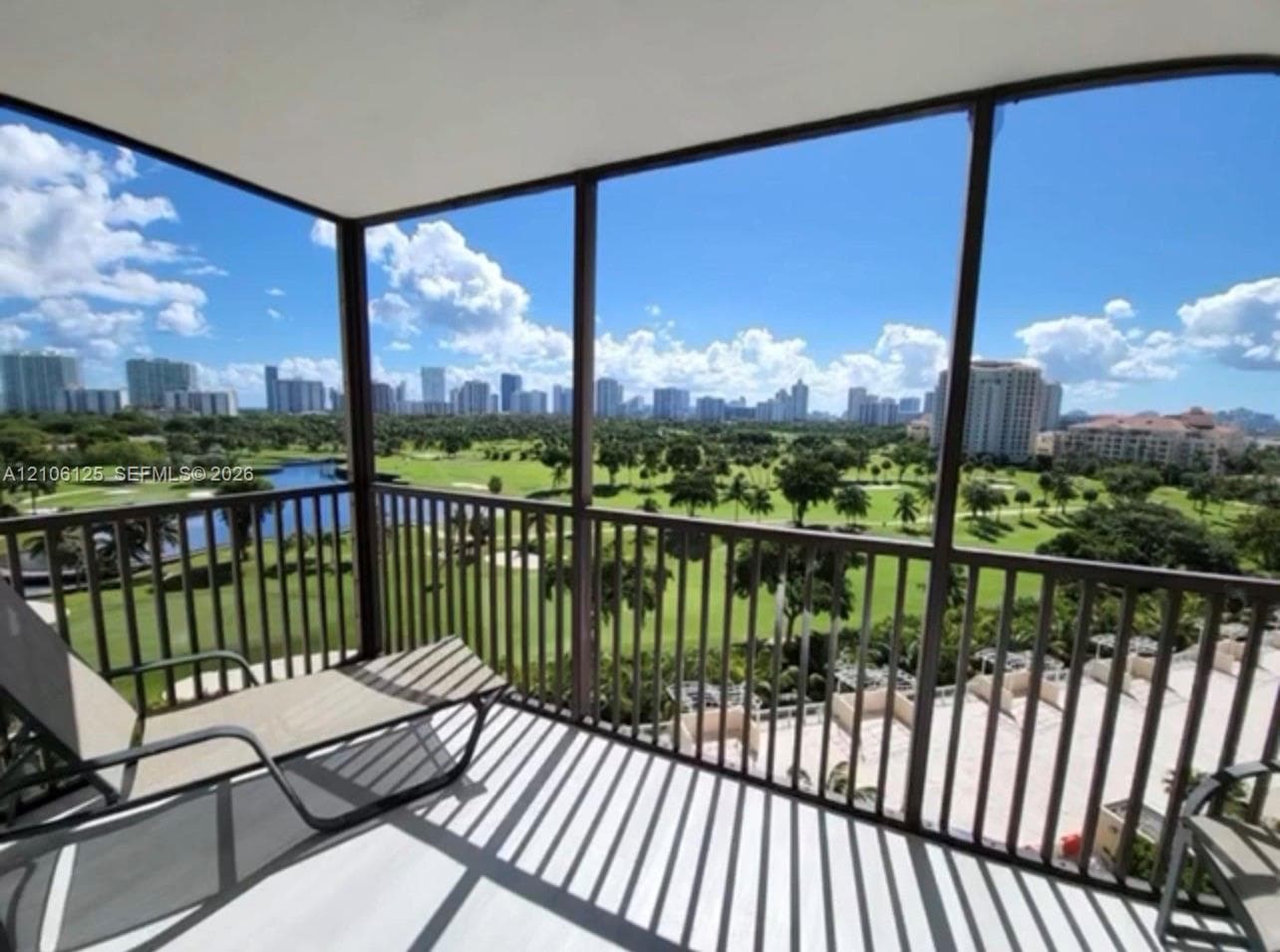 Covered balcony featuring screen enclosures and metal railings, overlooking a golf course and skyline