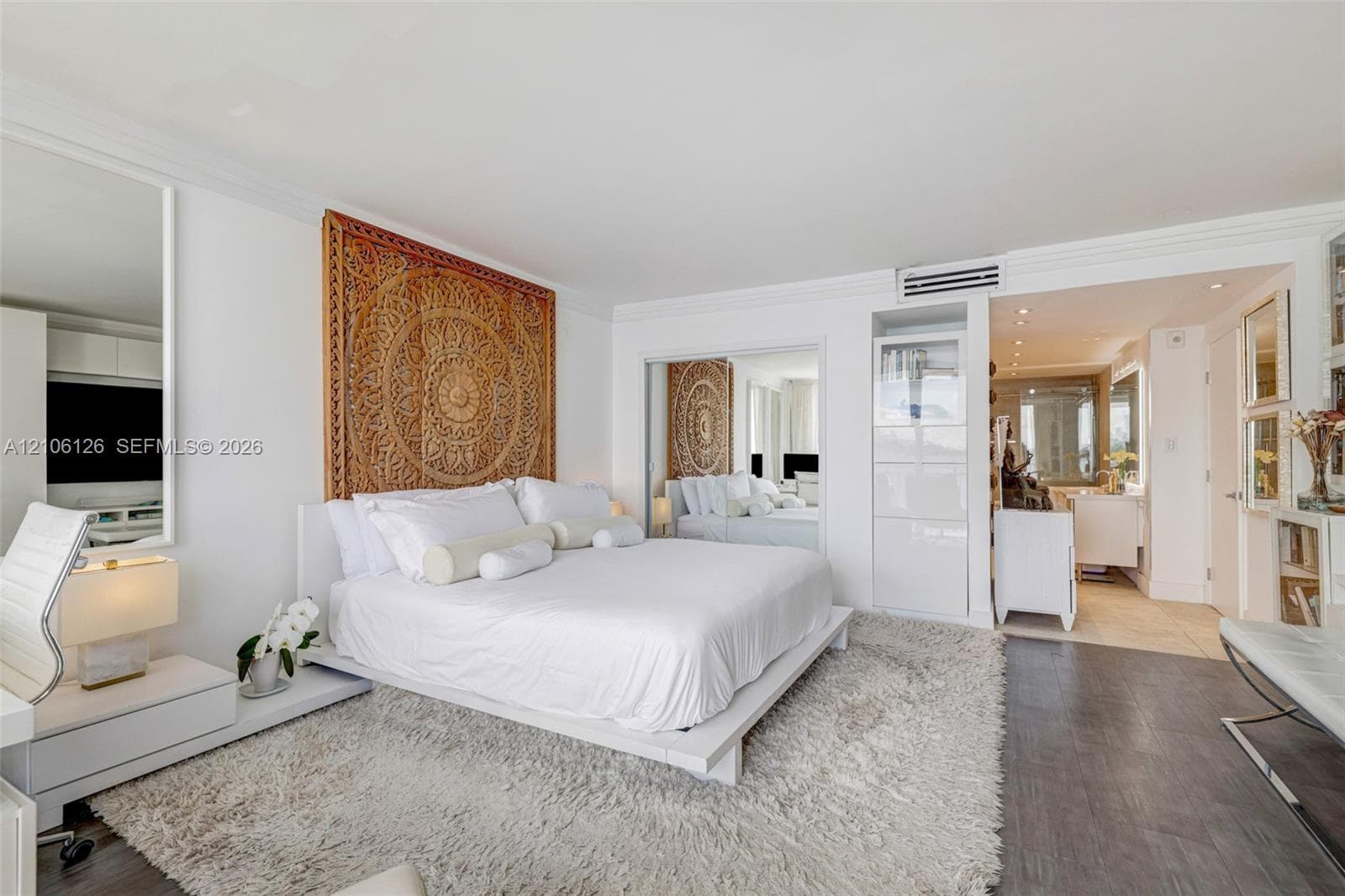 Floor-to-ceiling sliding glass doors, white tile flooring, and a private balcony featuring a water-front backdrop