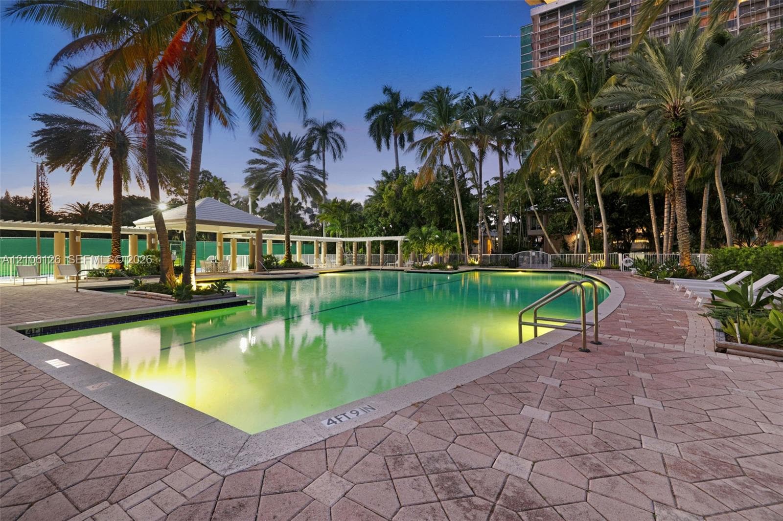 Outdoor recreation area featuring pedestal-mounted charcoal grills, paved walkway, manicured lawn, and mature palm trees
