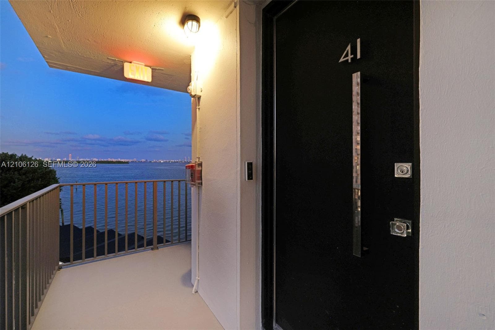 Covered balcony with a metal railing, floor-to-ceiling glass sliding doors, and water scenery