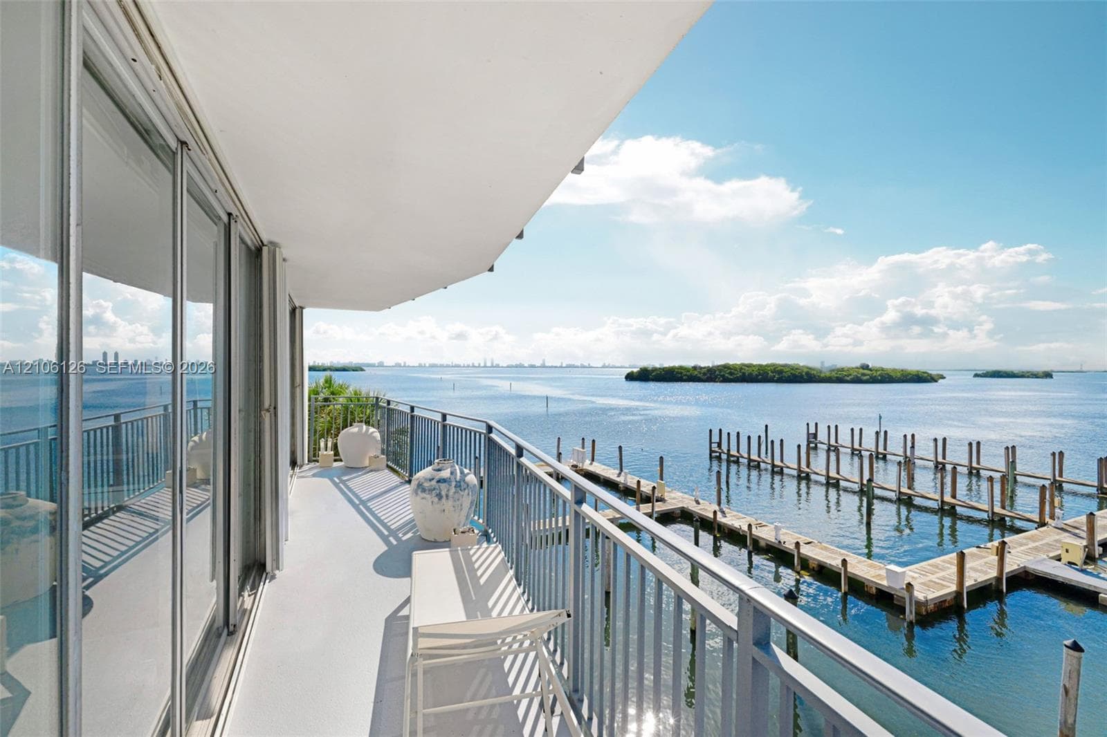 Covered balcony with a protective metal railing, floor-to-ceiling glass sliding doors, and water frontage featuring a private dock system