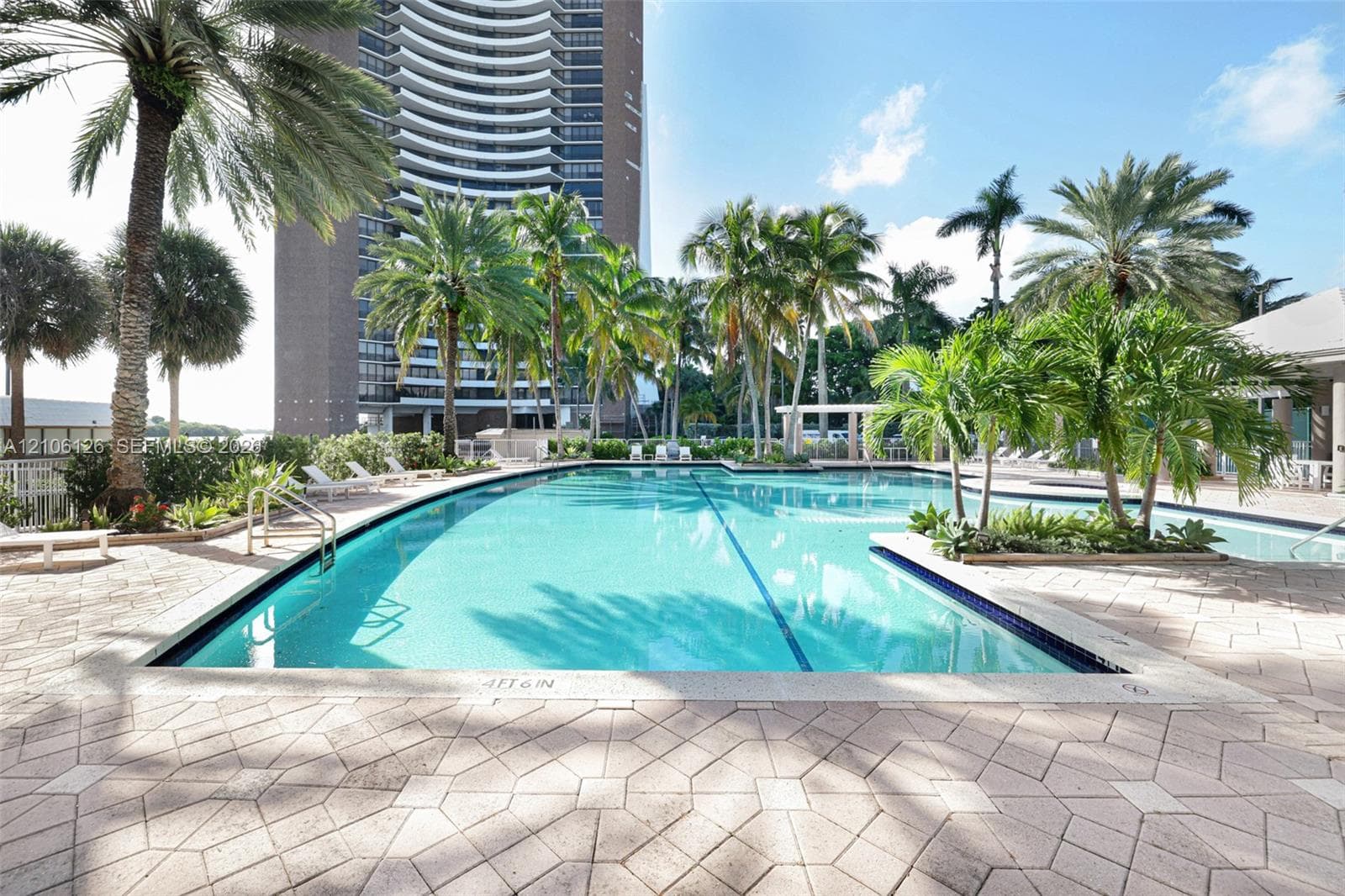 Swimming pool with integrated spa and decorative stone paver decking, surrounded by mature palm trees and a shaded pergola structure