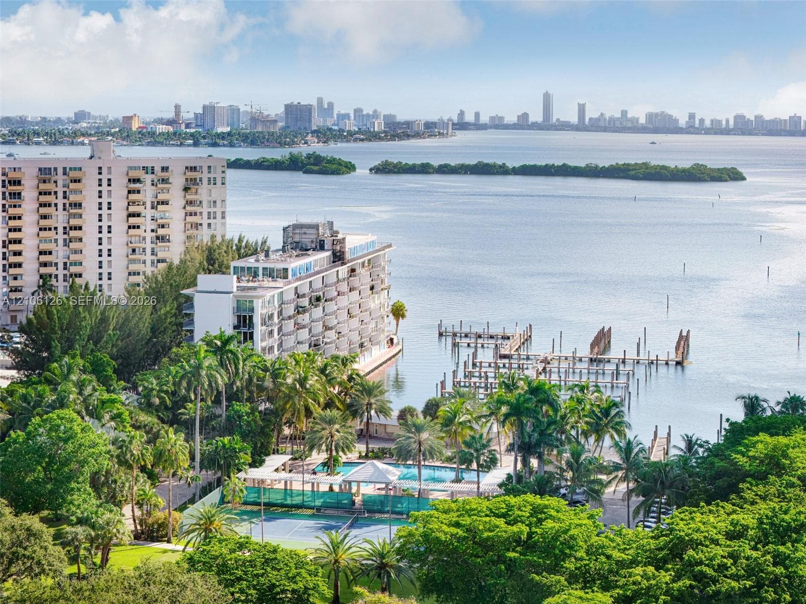 Waterfront complex featuring a private boat dock, outdoor swimming pool, tennis court, and mature tropical landscaping