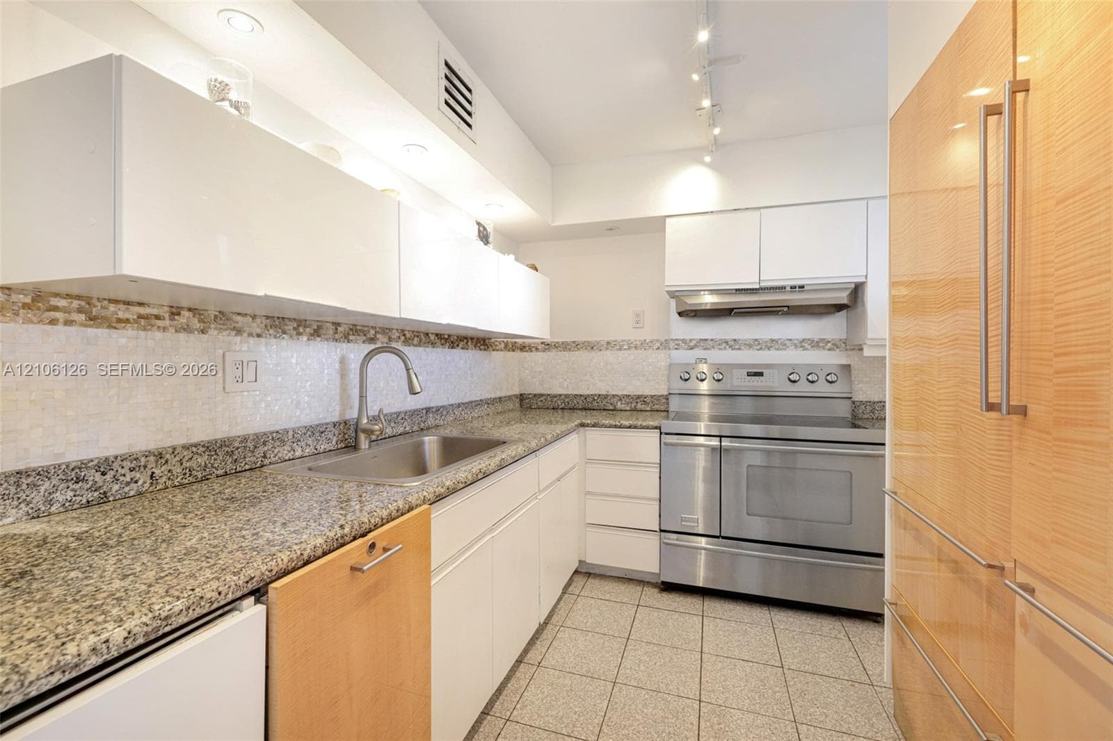 Kitchen featuring speckled stone countertops, high-gloss white cabinetry, integrated stainless steel appliances, a mosaic tile backsplash, and light-tone wood-finish cabinetry