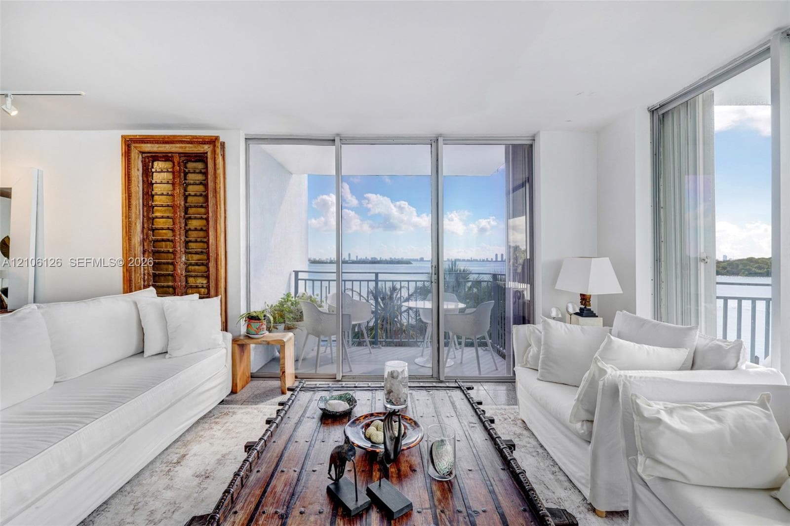 Floor-to-ceiling glass sliding doors, private balcony, water backdrop, and white walls