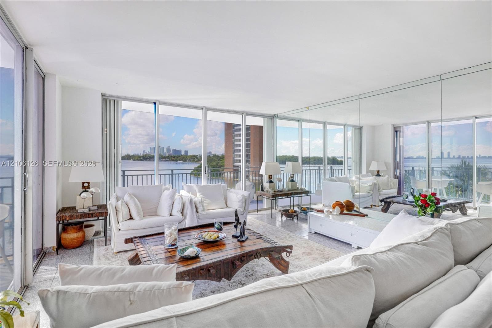 Floor-to-ceiling glass walls, integrated mirrored wall panels, stone-finish flooring, and private balcony access with water backdrop