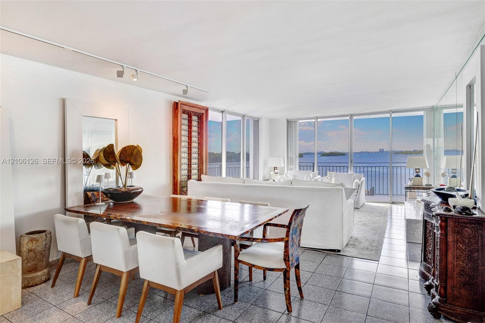 Open-concept living space featuring floor-to-ceiling windows, panoramic water scenery, polished stone-tile flooring, and adjustable ceiling-mounted track lighting