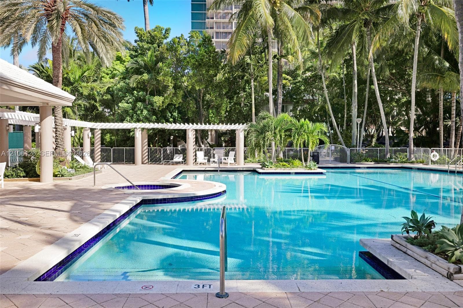 Swimming pool featuring a geometric paver deck, submerged step entry, and mature tropical landscaping