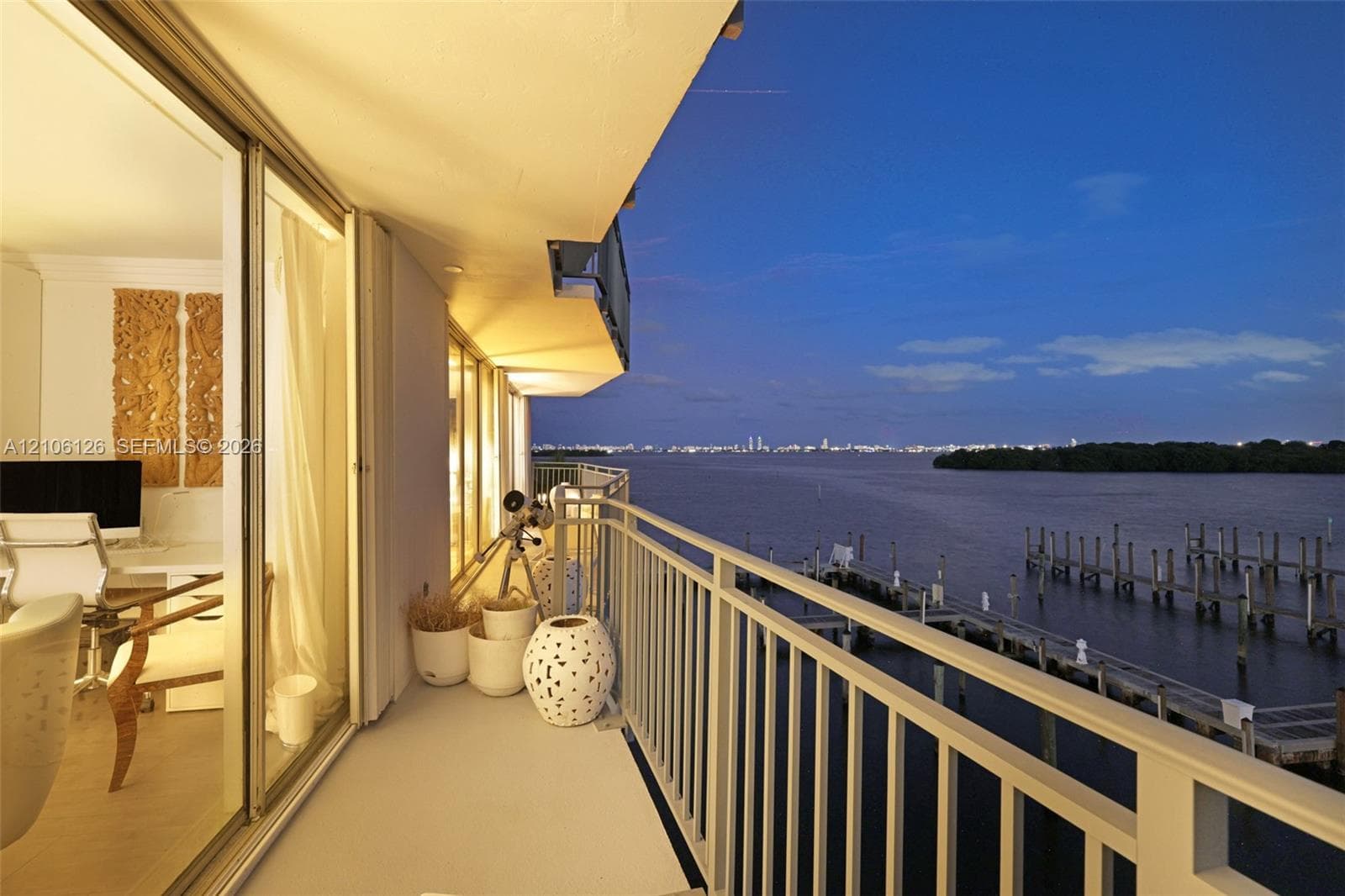 Elevated balcony featuring a white railing, overlooking open water and a distant cityscape skyline
