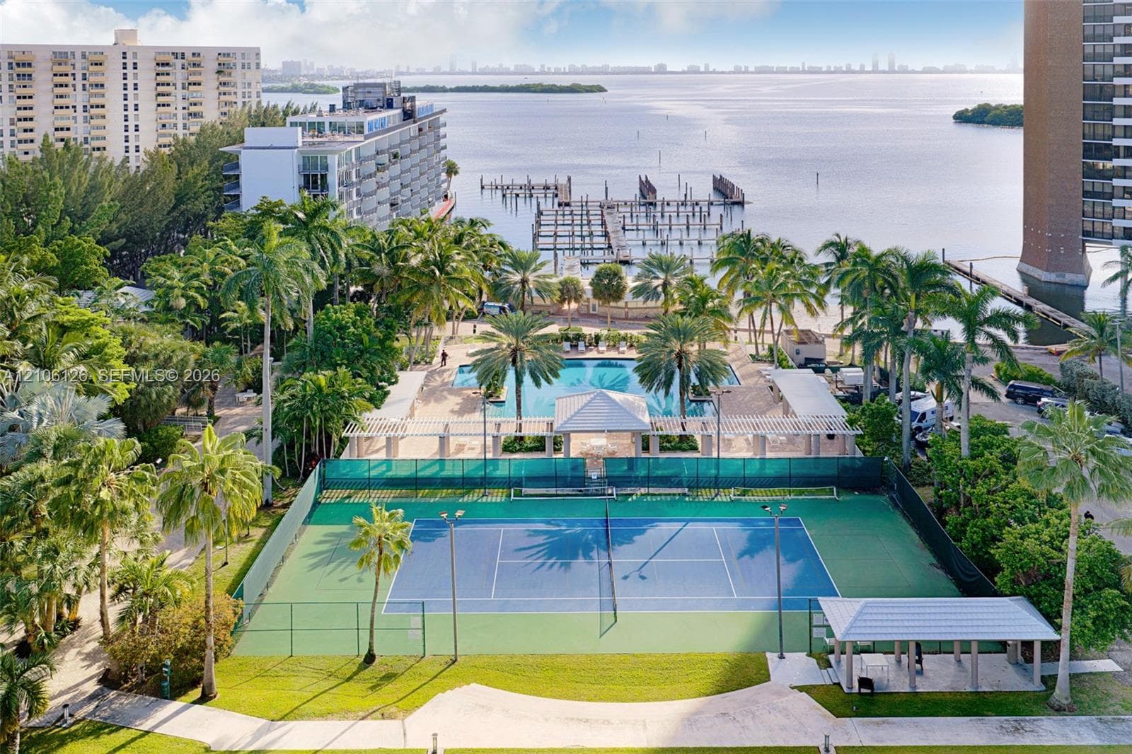 Waterfront property featuring a private marina with multiple boat slips, a swimming pool, a tennis court, and expansive landscaped grounds