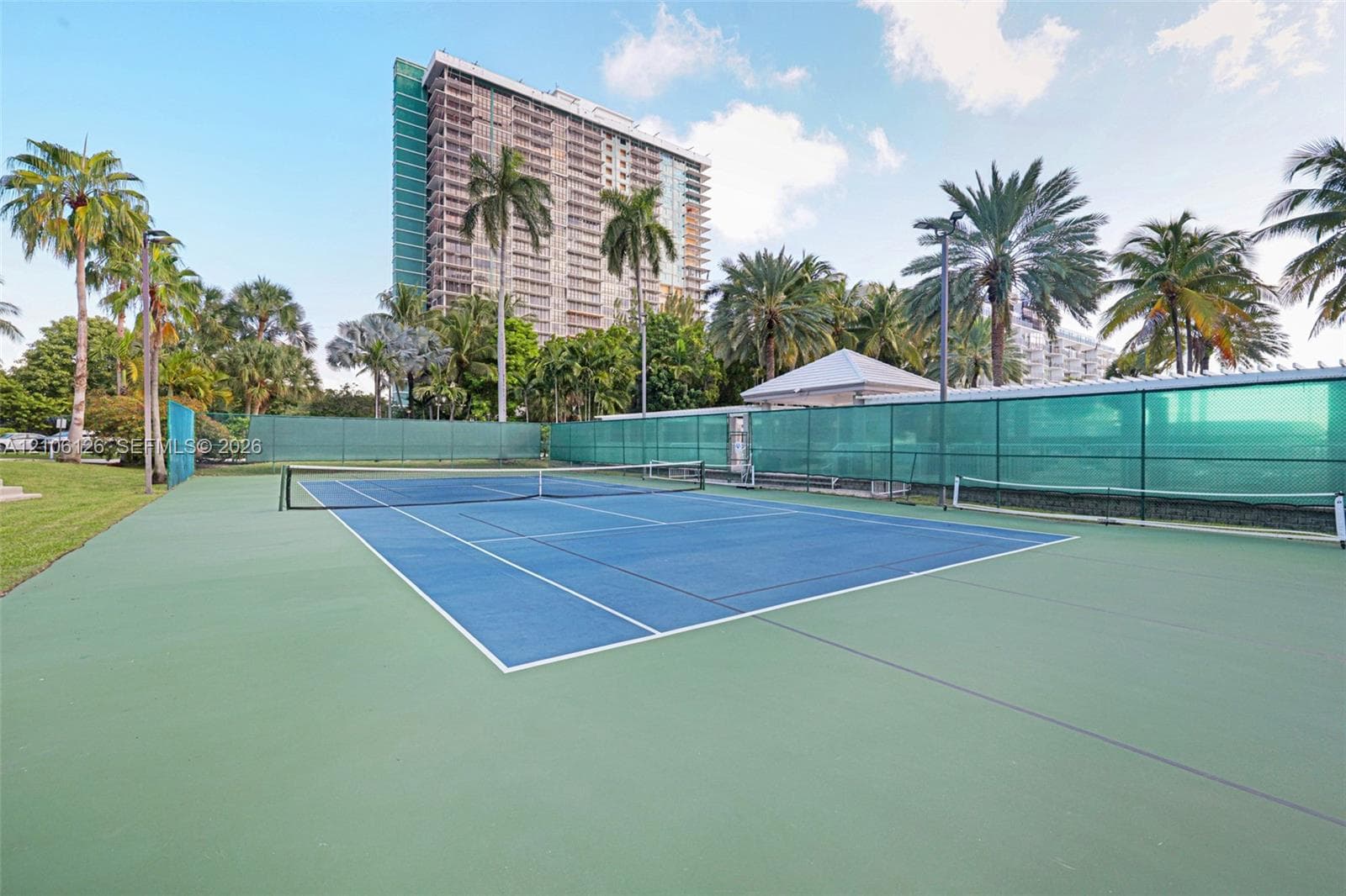 Tennis court featuring a hard surface with green and blue court markings, perimeter fencing, and integrated lighting fixtures