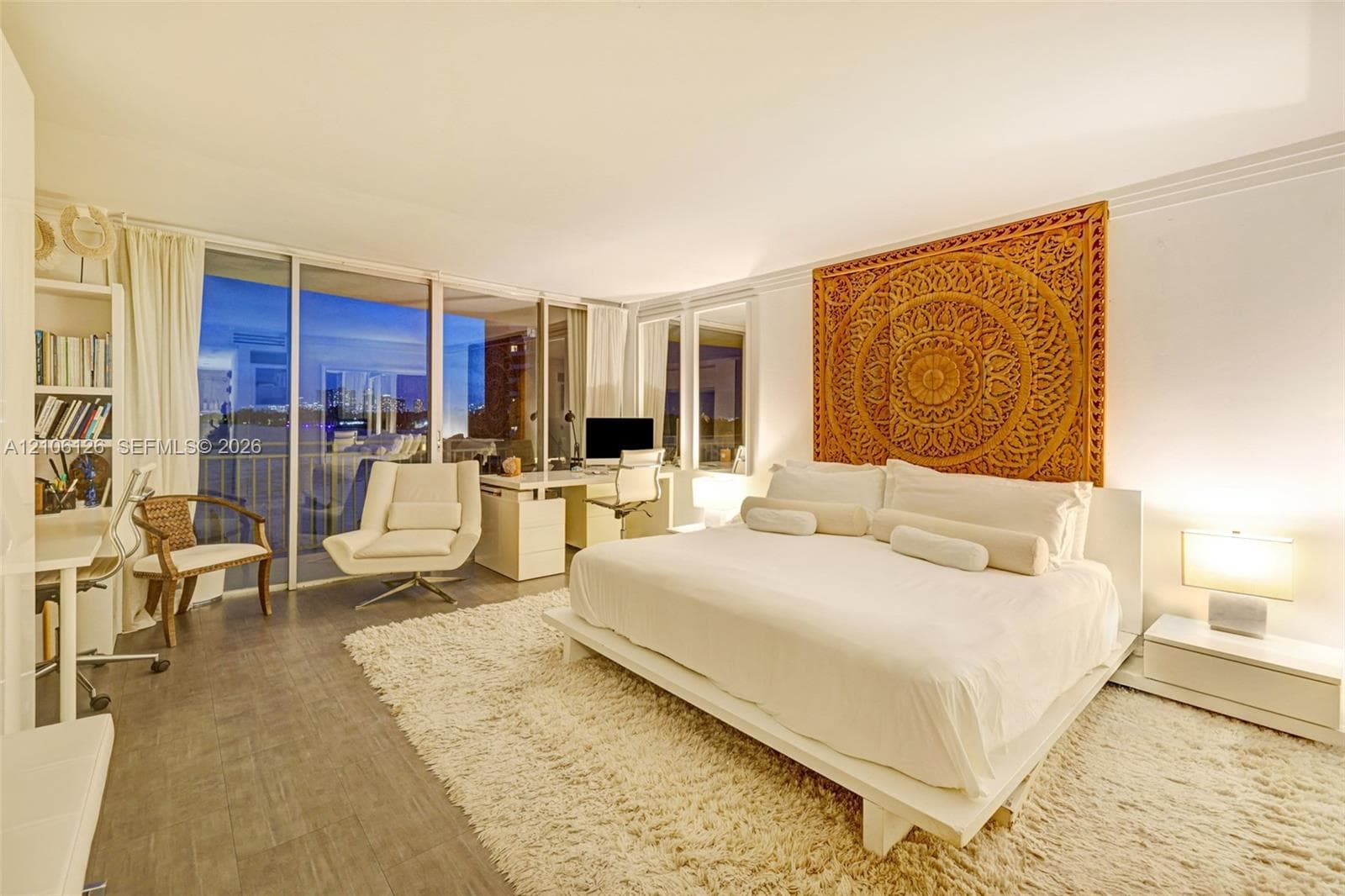 Floor-to-ceiling glass windows, wood-finish flooring, built-in cabinetry with integrated shelving, and a balcony featuring a water backdrop