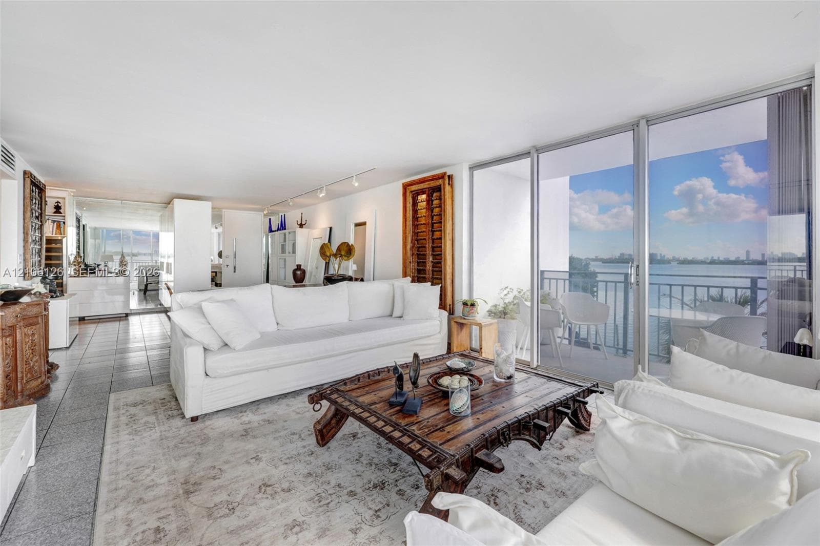 Floor-to-ceiling sliding glass doors, ceramic tile flooring, built-in track lighting, and a private balcony featuring an aluminum railing overlooking the water