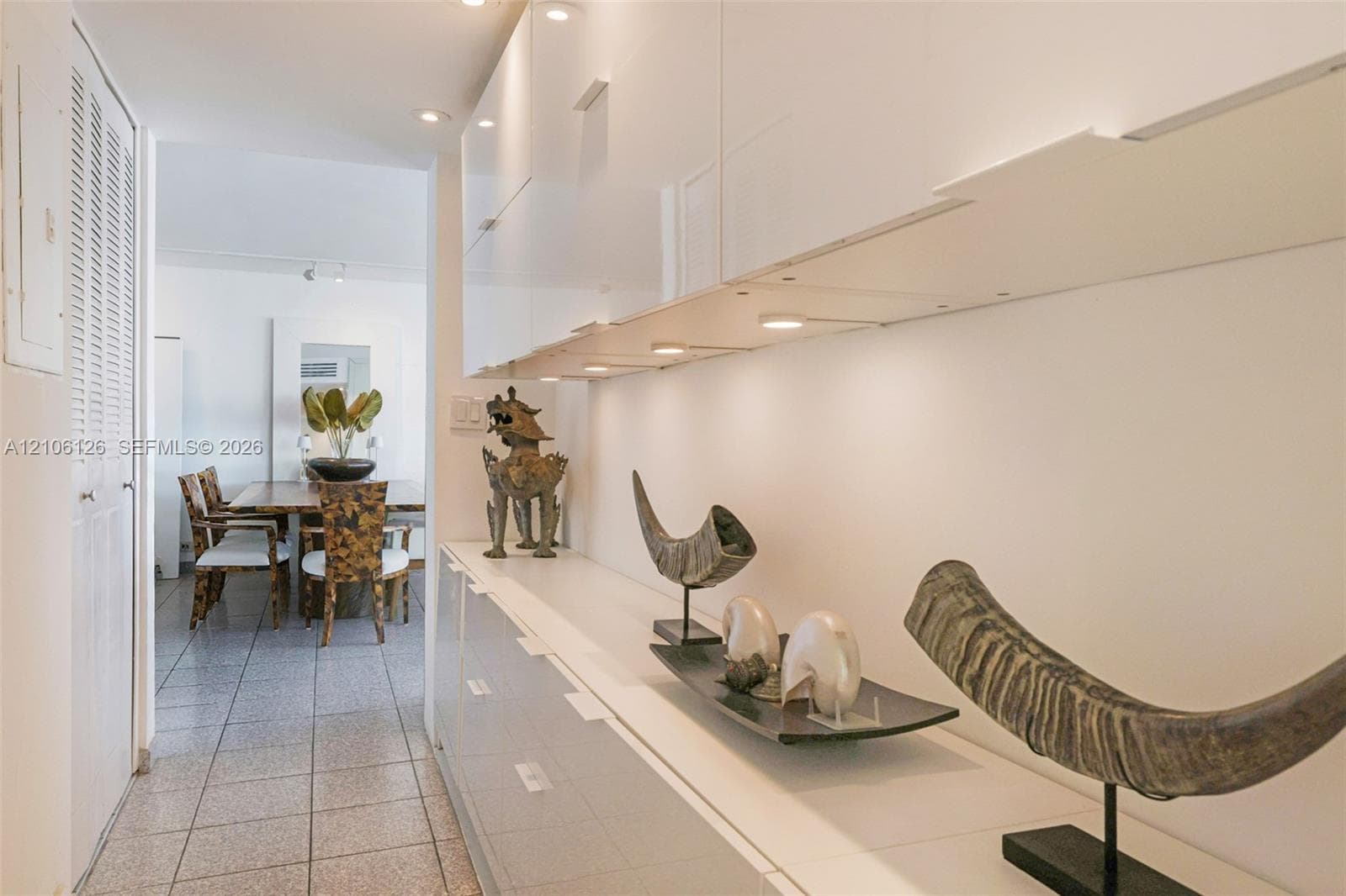 Hallway featuring high-gloss white built-in cabinetry, recessed ceiling lighting, tile flooring, and louvered double-door closet