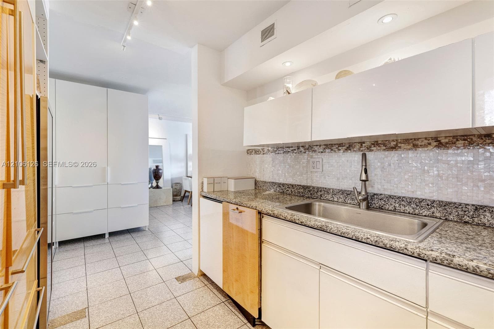 Kitchen featuring white flat-panel cabinetry, stone countertops, stainless steel undermount sink with a gooseneck faucet, mosaic tile backsplash, and light-toned ceramic tile flooring