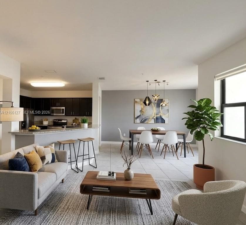Open-concept space featuring tile flooring, a kitchen peninsula with stone-surface countertop, dark wood cabinetry, and a multi-light pendant fixture