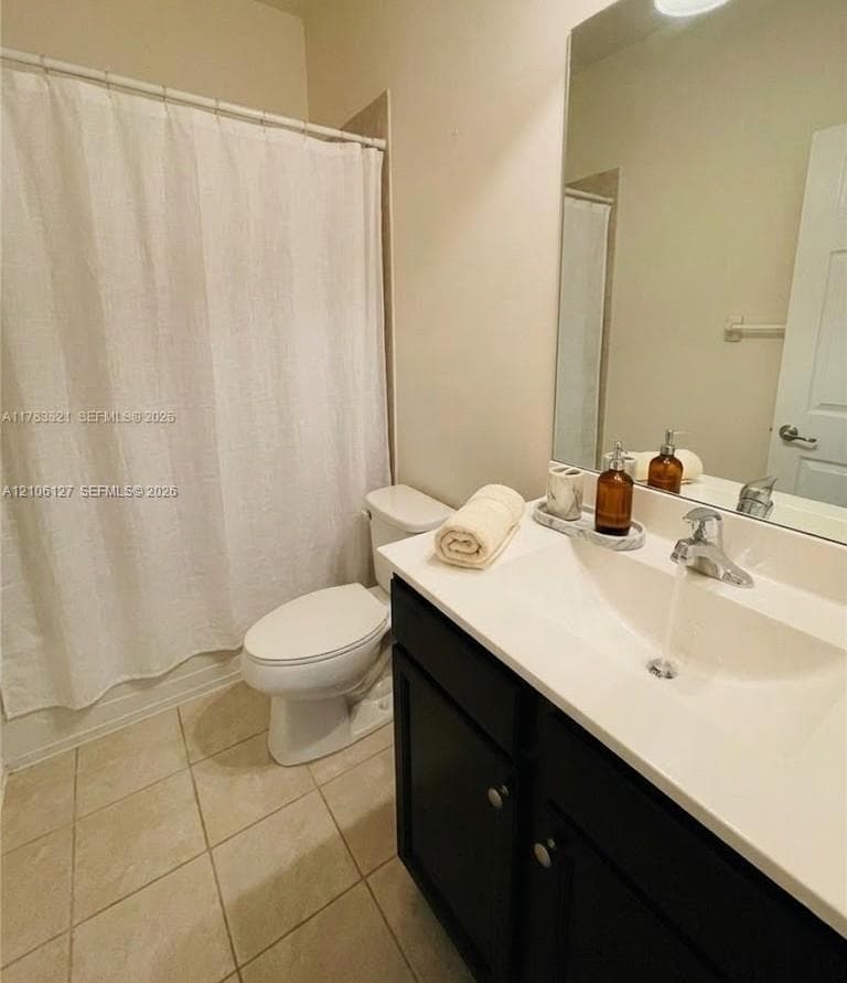 Full bathroom featuring a dark-finish vanity with a white countertop, integrated sink, large wall-mounted mirror, and tile flooring