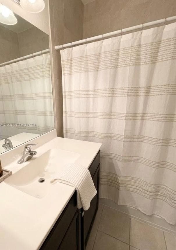 Bathroom featuring a dark wood-finish vanity, solid-surface countertop with an integrated sink, polished chrome faucet, full-width mirror, and neutral floor tile