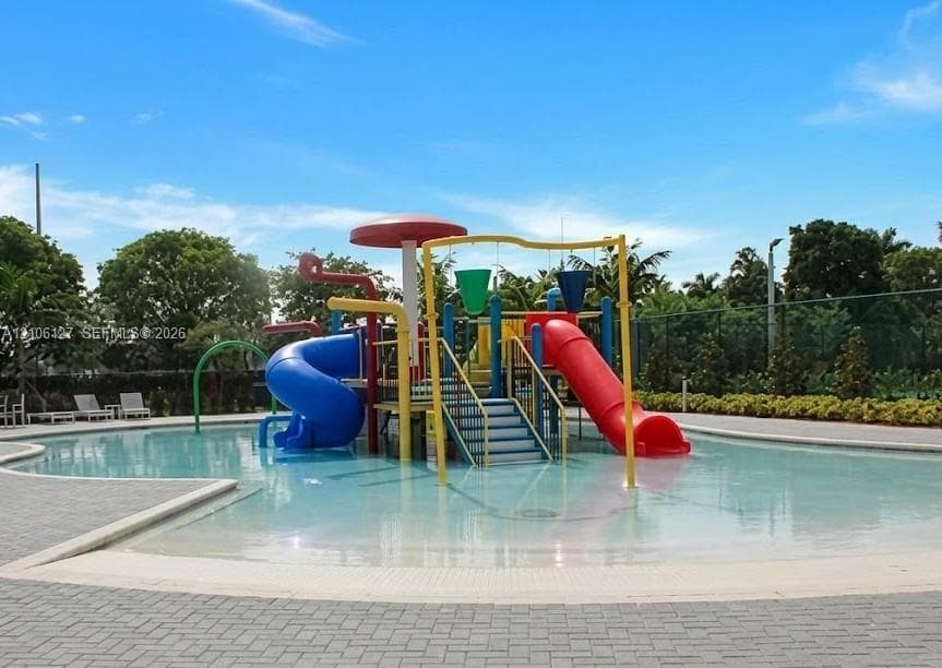 Zero-entry swimming pool featuring a central aquatic play structure with dual slides, overhead water features, and a perimeter paved deck