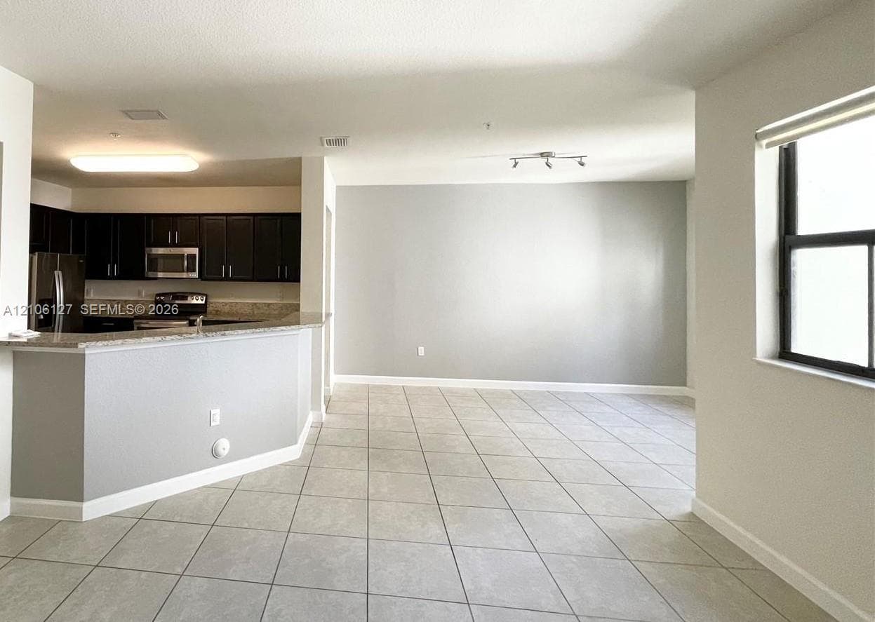 Kitchen featuring dark cabinetry, stone-finish countertops, stainless steel appliances, neutral tile flooring, and a peninsula counter