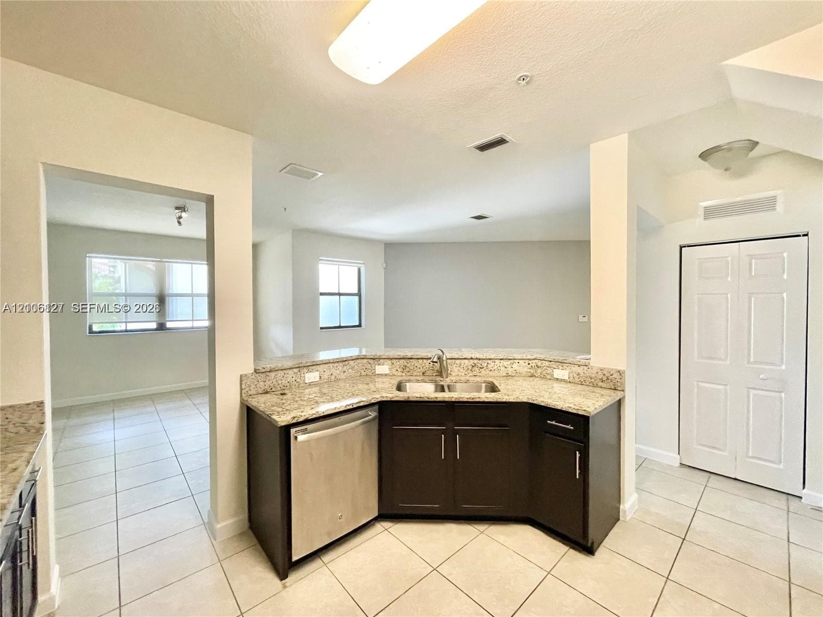 Kitchen area featuring dark cabinetry, stone-surface countertops, dual-basin stainless steel sink, stainless steel dishwasher, and tile flooring