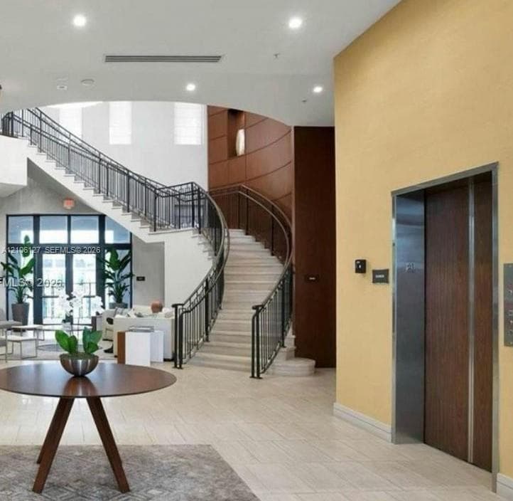 Grand foyer featuring a curved staircase with metal railing, stone-finish flooring, recessed lighting, and a stainless steel elevator with wood-panel door
