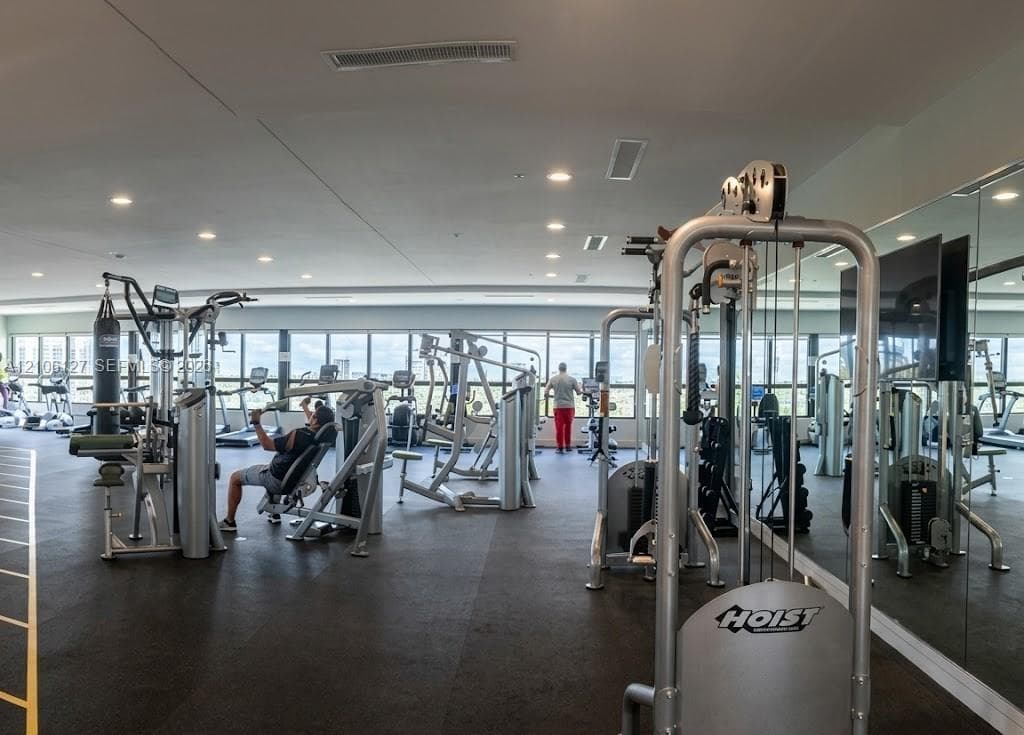 Fitness center featuring high-impact rubber flooring, full-wall mirrors, recessed lighting, and expansive floor-to-ceiling windows