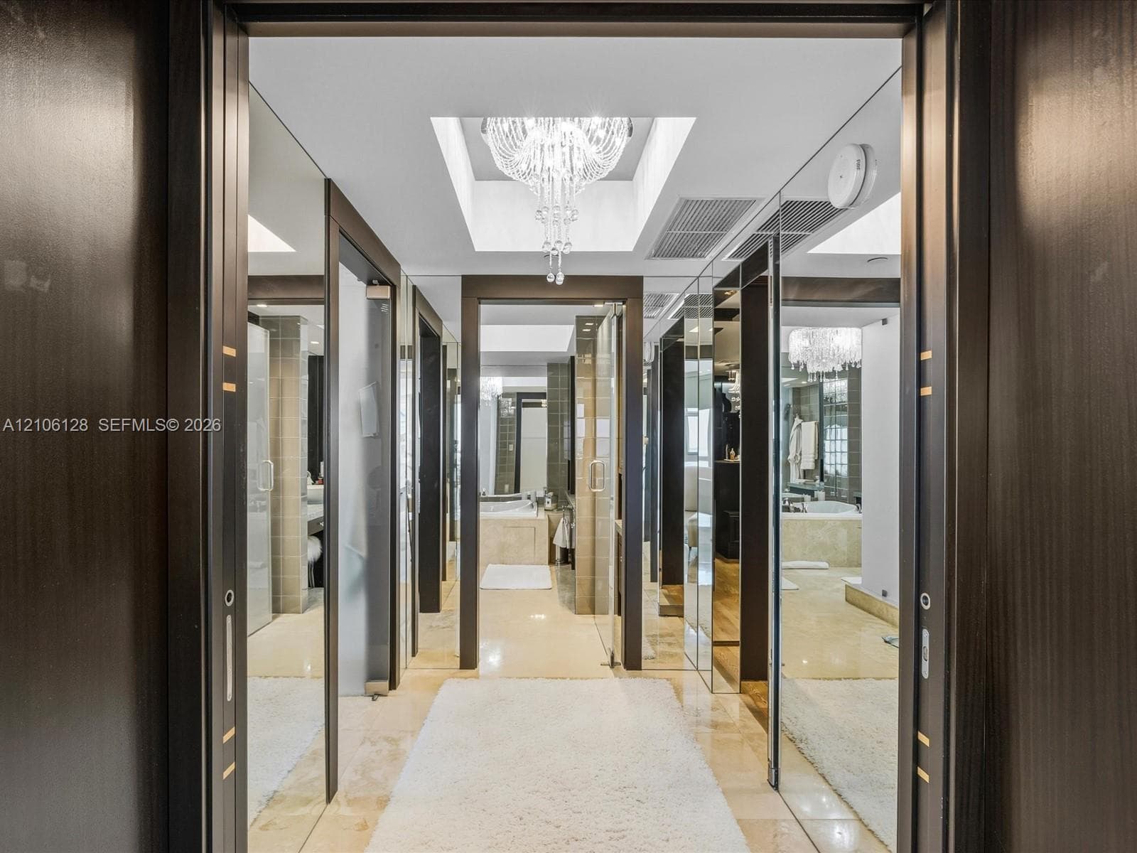 High-gloss dark wood doorways with metal inlay, full-length mirror paneling, recessed lighting, and a crystal chandelier