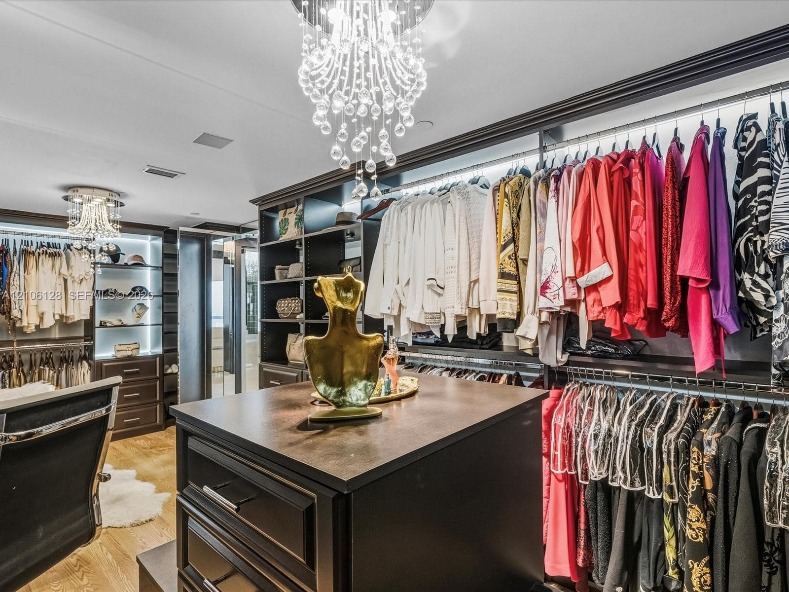 Custom walk-in closet featuring built-in dark wood cabinetry, integrated LED shelf lighting, a center island with a dark countertop, and decorative crystal chandeliers
