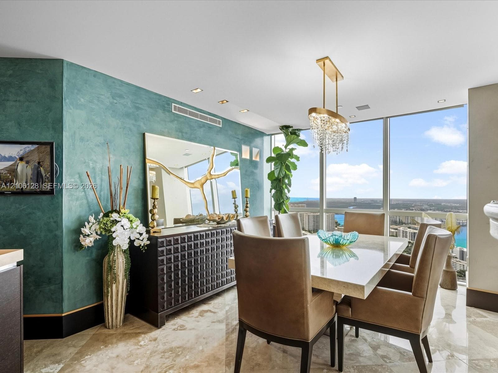 Dining area featuring floor-to-ceiling windows, polished stone flooring, custom textured wall finish, and a suspended crystal chandelier