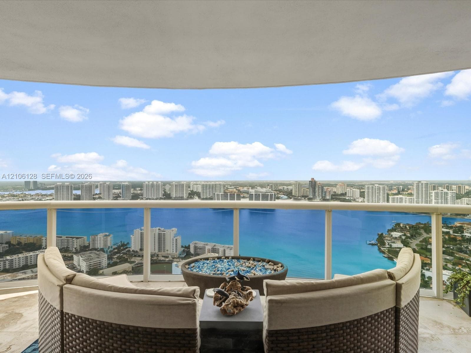 Covered private balcony featuring stone flooring and a glass railing with panoramic water and skyline scenery