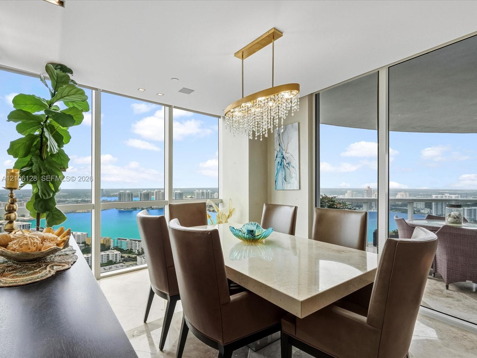 Floor-to-ceiling windows, crystal chandelier, and light-toned flooring featuring a expansive balcony and panoramic water exposure