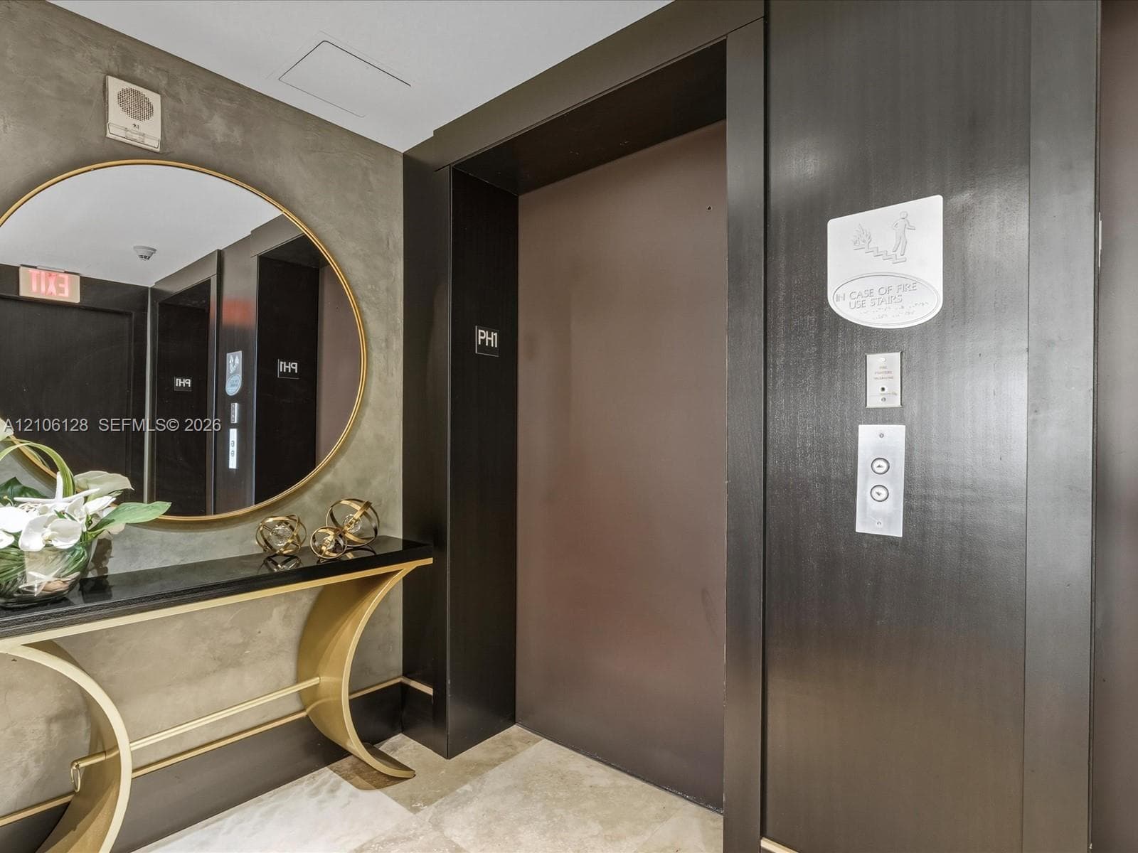Elevator lobby featuring custom dark wood door surround, textured concrete-style wall finish, and stone flooring