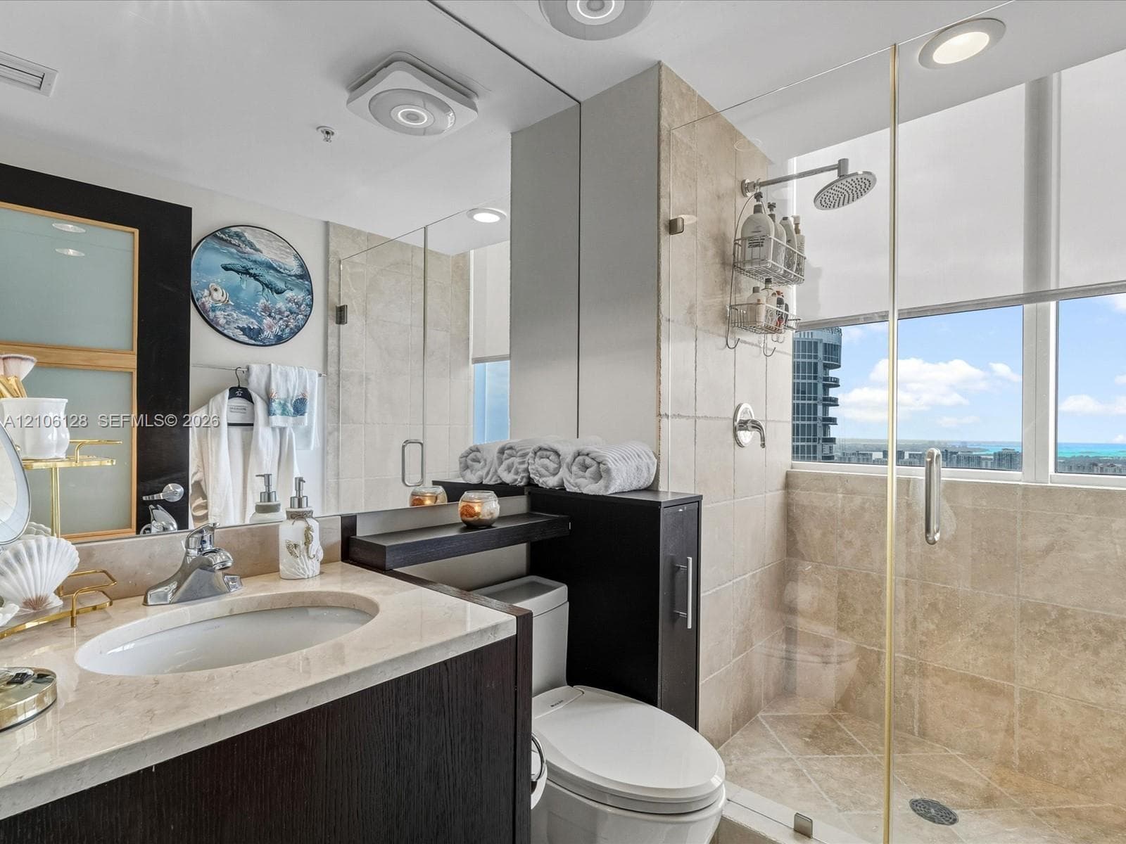 Bathroom featuring a stone-surface vanity with an integrated undermount sink, dark-finish cabinetry, floor-to-ceiling tile shower enclosure, glass partition, and full-width vanity mirror