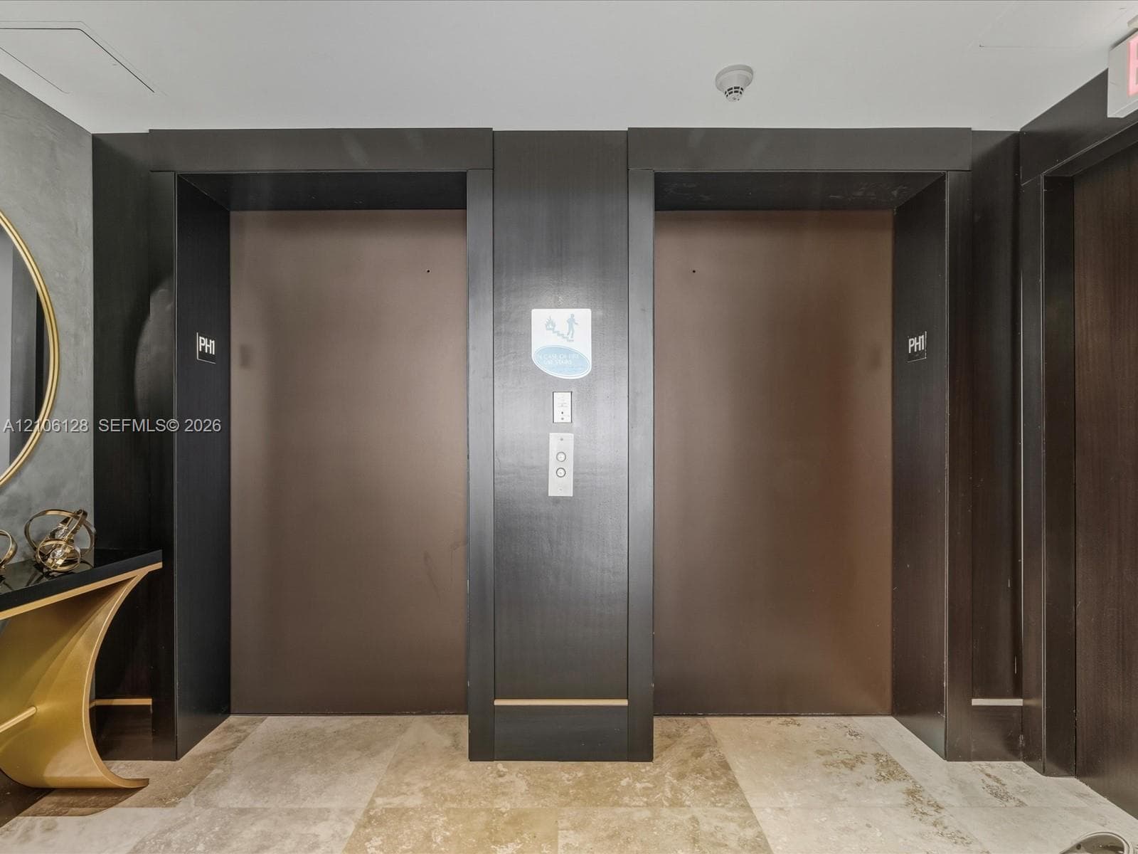 Dual elevators with dark matte metallic doors and surrounds, set against a stone tile floor