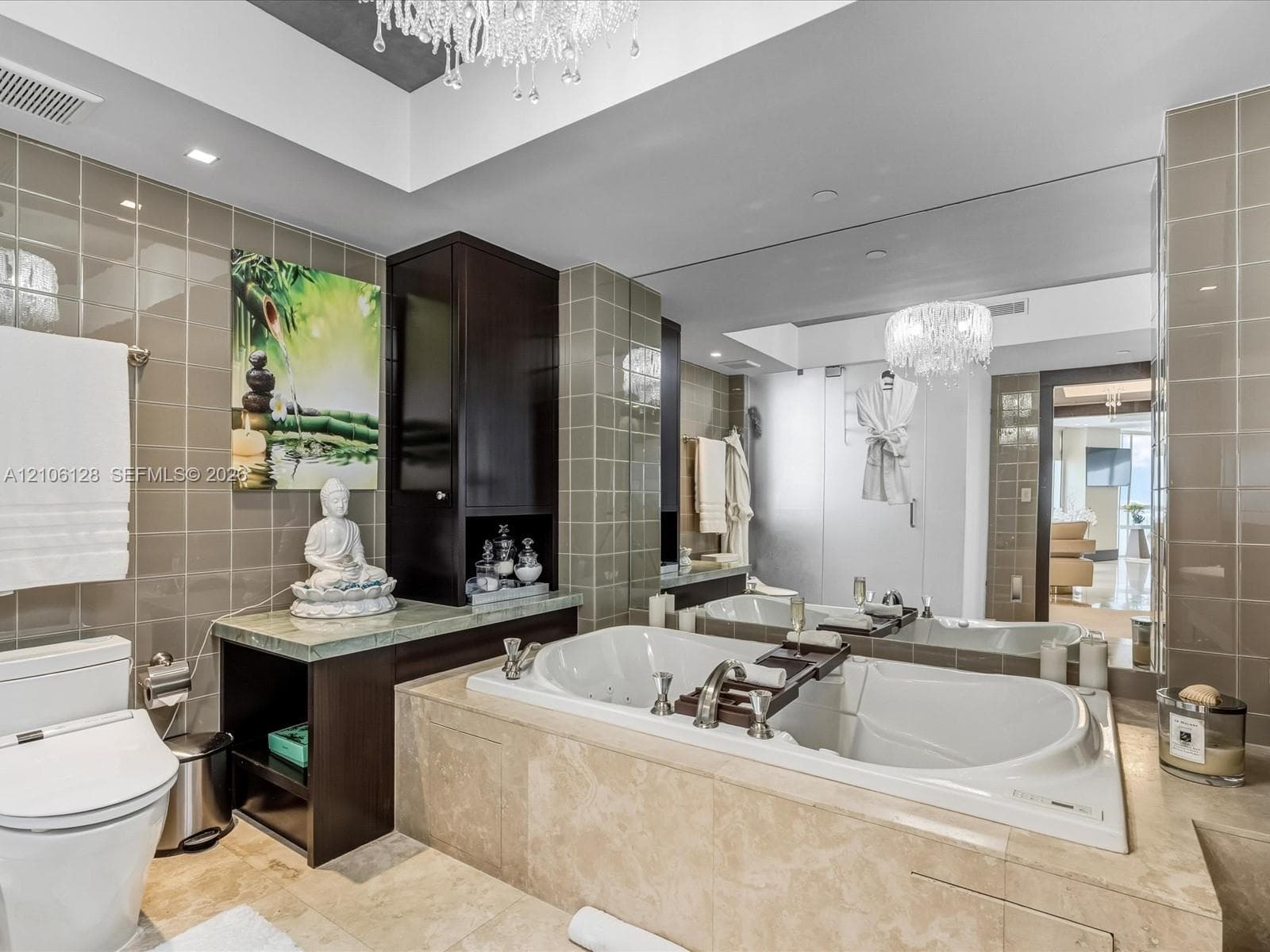 Bathroom featuring a stone-encased jetted soaking tub, dark-finish cabinetry with an integrated countertop, wall-to-wall mirror, tiled walls, and a crystal chandelier