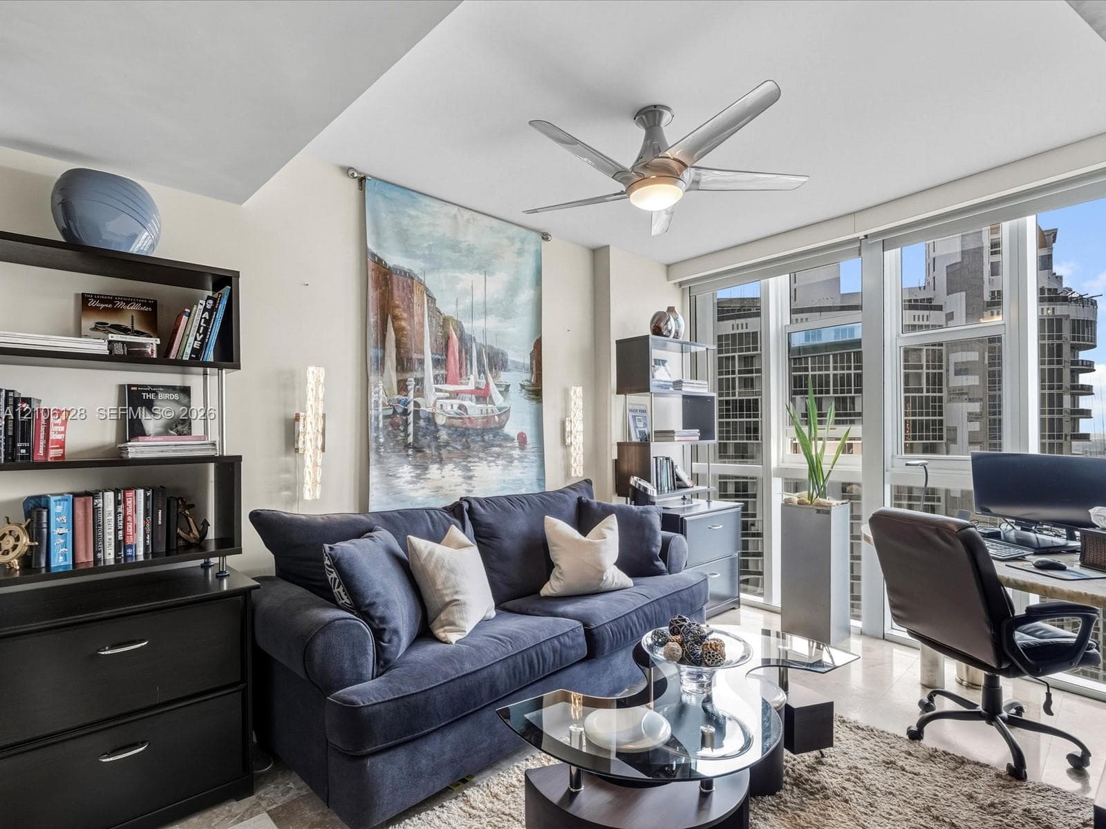 Floor-to-ceiling windows, recessed ceiling detail, brushed metal ceiling fan, and vertically mounted wall sconces