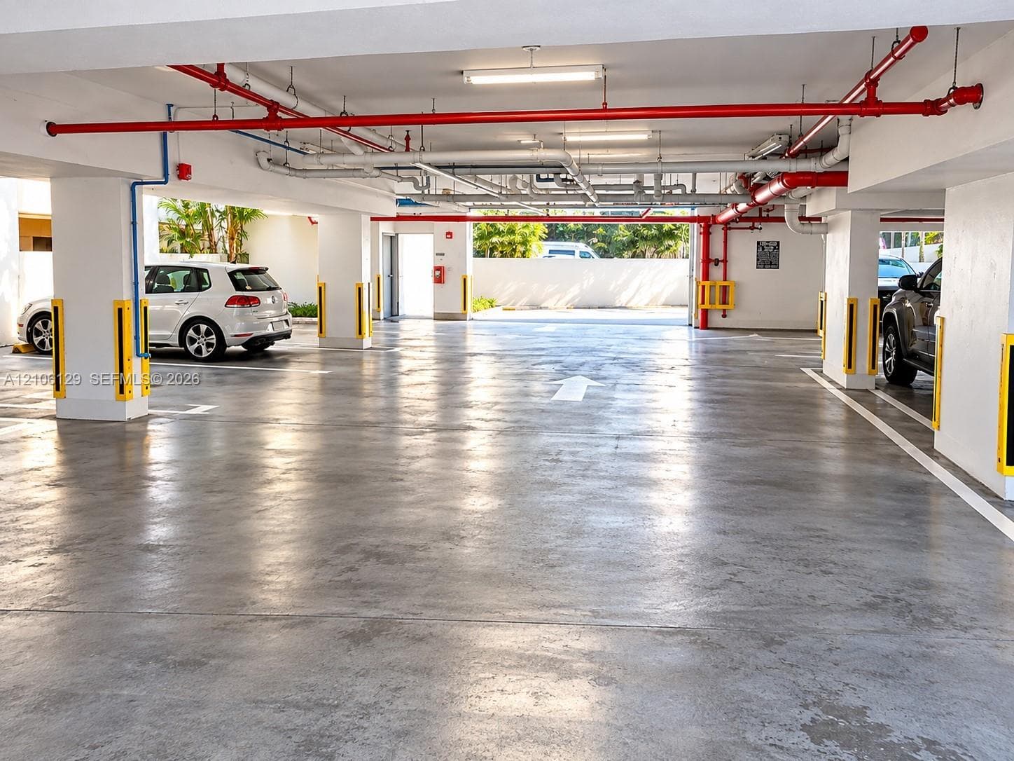 Covered parking garage featuring smooth concrete flooring, structural concrete support columns, and overhead fluorescent lighting