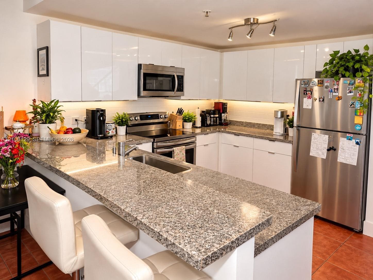 Kitchen featuring high-gloss white cabinetry, stone-finish countertops, stainless steel appliances, and integrated under-cabinet lighting