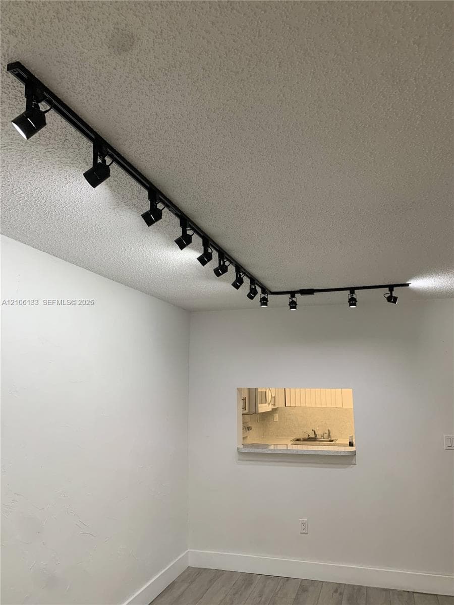 Ceiling-mounted matte black track lighting system featuring multiple adjustable spotlights, complemented by a service pass-through opening with a countertop ledge and wood-finish flooring