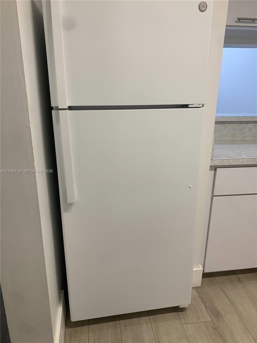 White top-mount refrigerator paired with cabinetry featuring light-toned countertops and wood-finish flooring