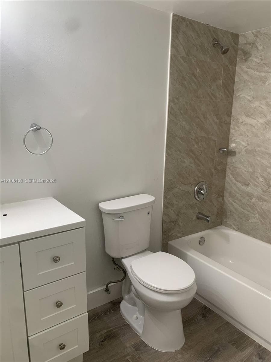 White vanity with multiple storage drawers, wood-finish flooring, and a bathtub with full-height stone-patterned tile surround