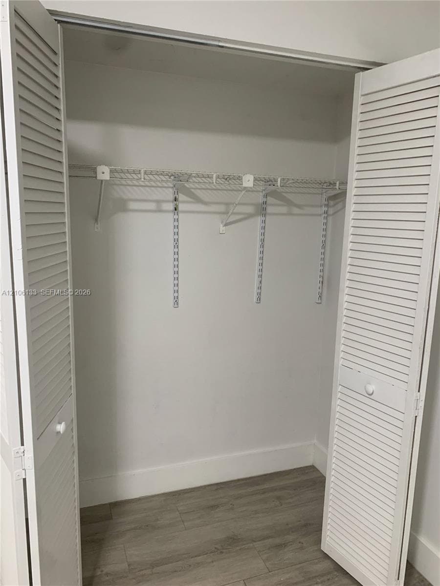 Storage closet featuring dual white louvered bi-fold doors, wood-finish flooring, and integrated wire shelving with a hanging rod